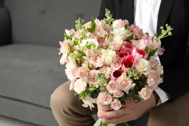 Photo of Man with beautiful bouquet of flowers on sofa indoors, closeup. Space for text