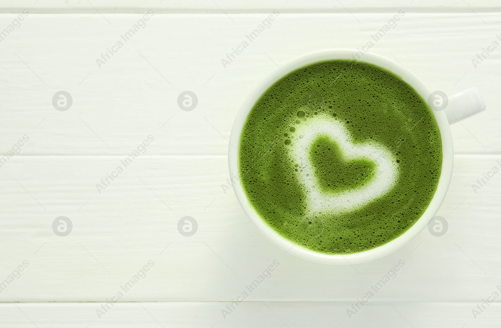 Photo of Cup of fresh matcha latte on white wooden table, top view. Space for text