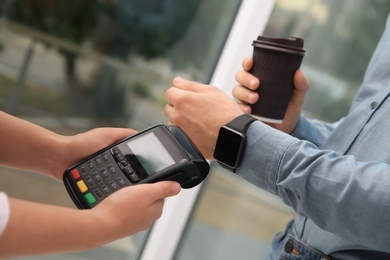 Photo of Man using smart watch for contactless payment via terminal in cafe, closeup