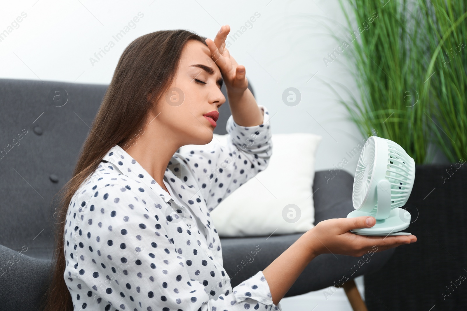 Photo of Woman with portable fan suffering from heat at home. Summer season