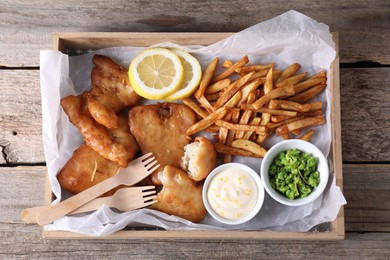 Photo of Tasty fish, chips, sauce and peas on wooden table, top view