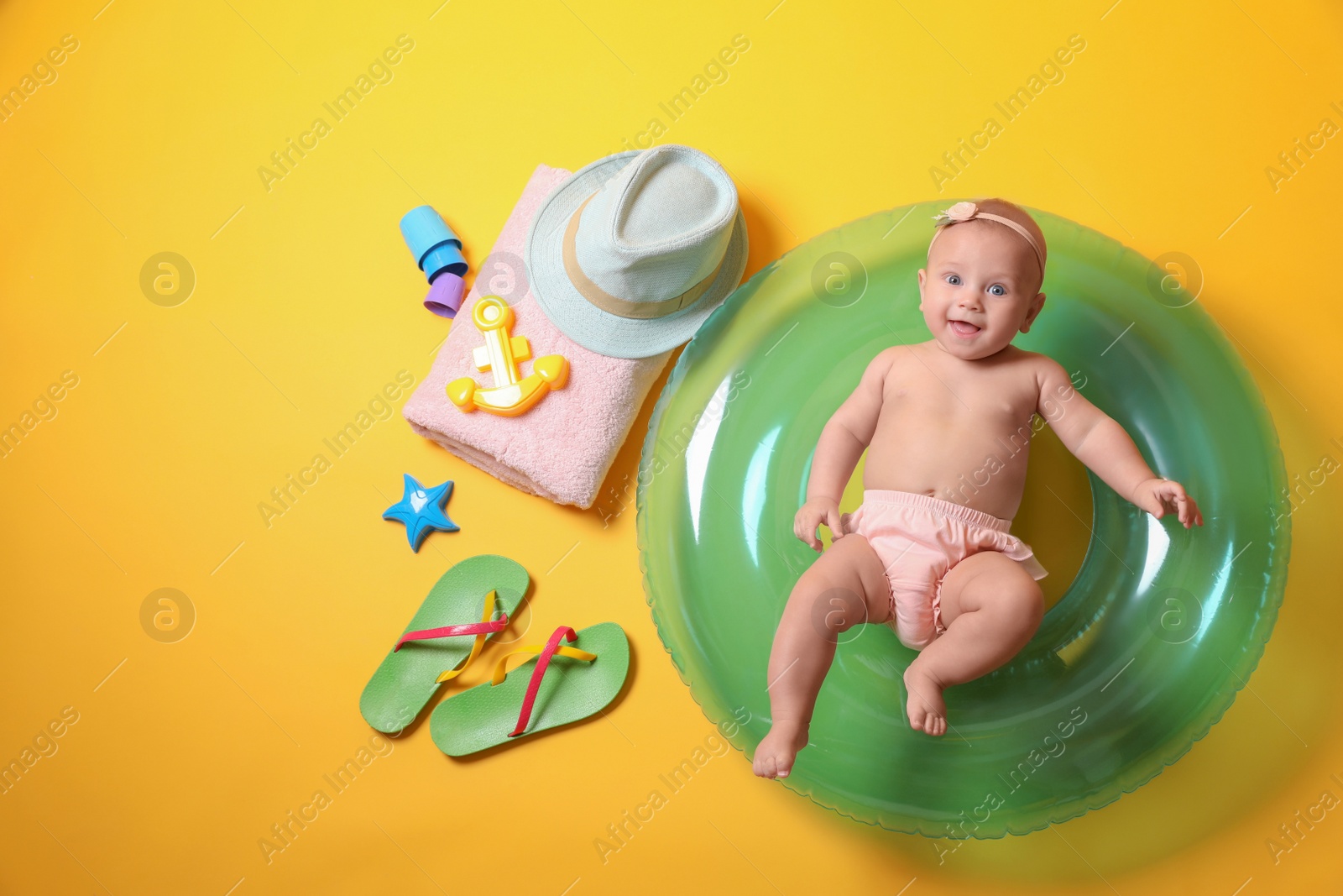 Photo of Cute little baby with inflatable ring and beach accessories on yellow background, top view