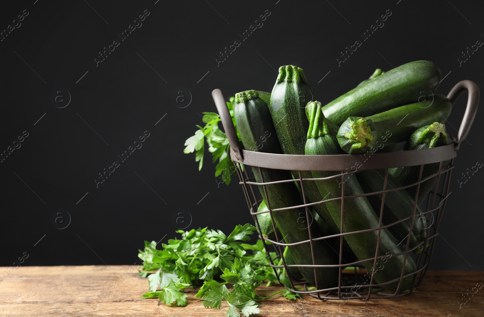Photo of Basket with green zucchinis and parsley on wooden table. Space for text
