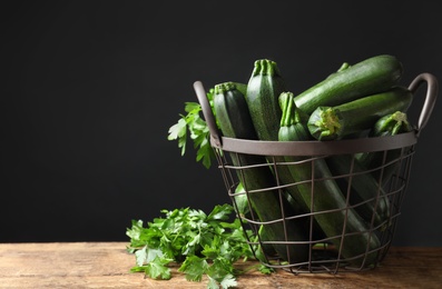 Basket with green zucchinis and parsley on wooden table. Space for text