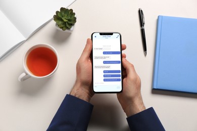 Image of Man texting via mobile phone at table, top view. Device screen with messages