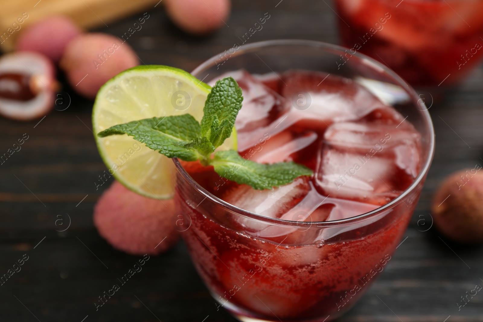 Photo of Lychee cocktail with lime, ice and mint on dark wooden table, closeup