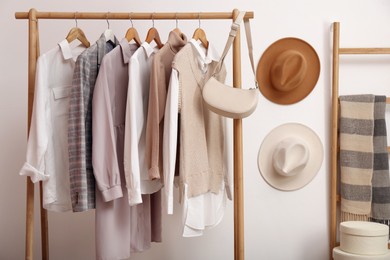 Rack with different stylish clothes and bag near white wall indoors