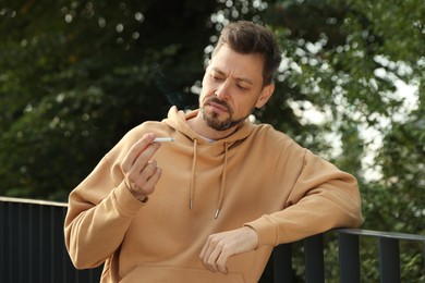 Photo of Man smoking cigarette near railing outdoors. Bad habit
