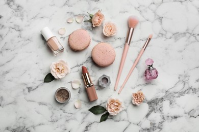 Flat lay composition with makeup products, roses and macarons on white marble background