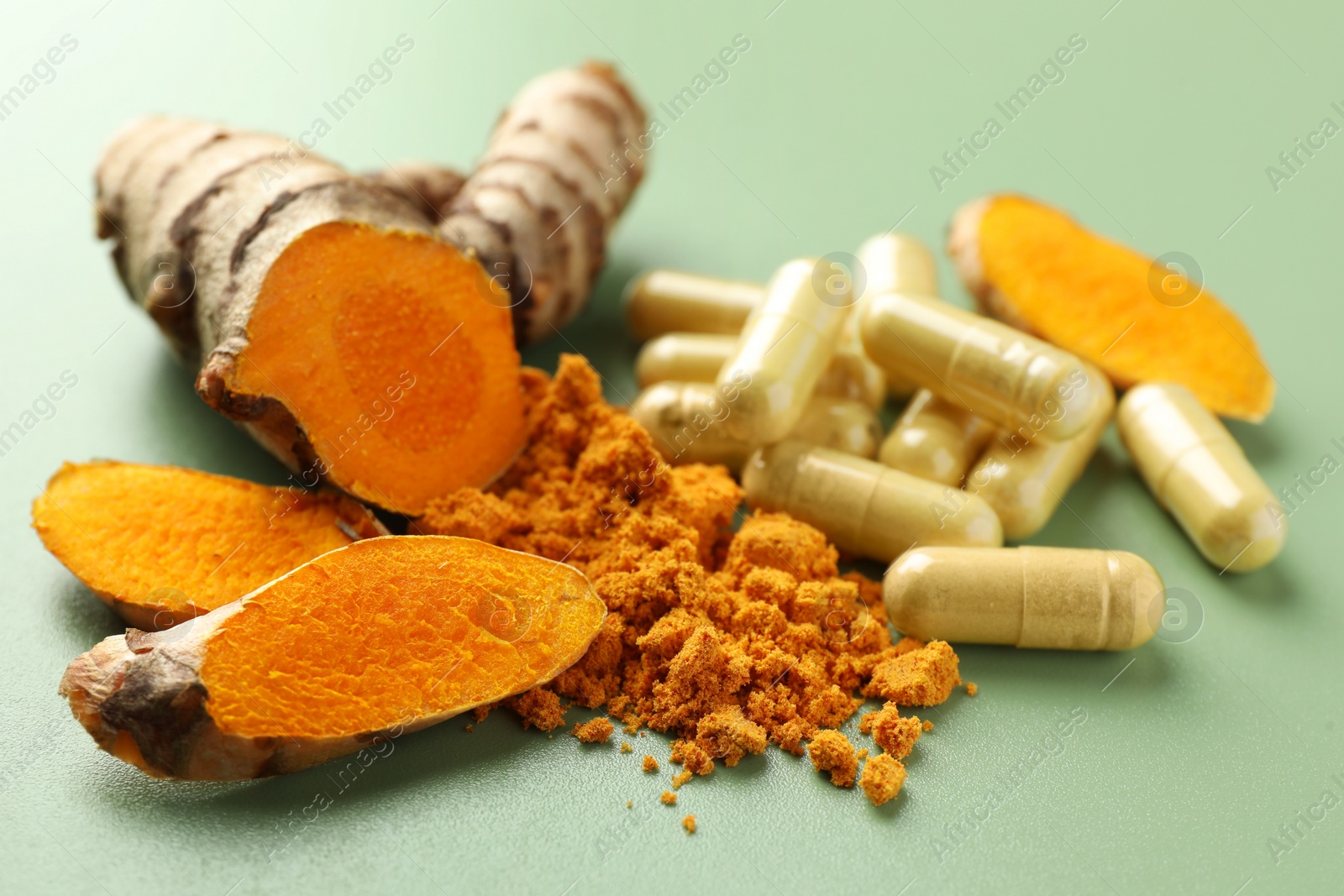 Photo of Aromatic turmeric powder, pills and raw roots on green background, closeup