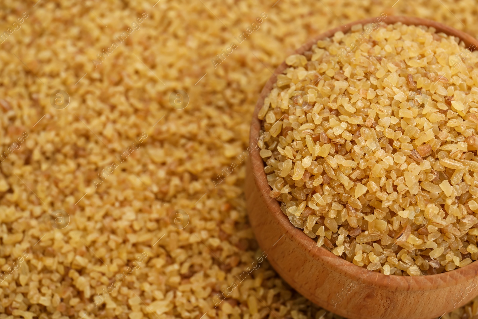 Photo of Wooden bowl on pile of uncooked bulgur, closeup. Space for text