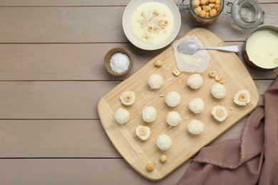 Photo of Delicious candies with coconut flakes, hazelnut and ingredients on wooden table, flat lay. Space for text