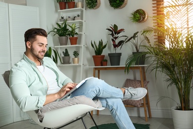 Young man reading book in room with different home plants