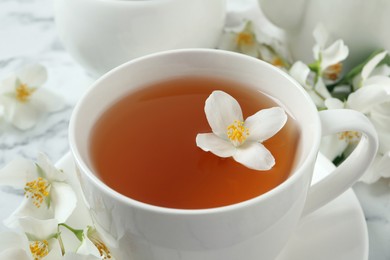 Cup of aromatic jasmine tea and fresh flowers on table, closeup