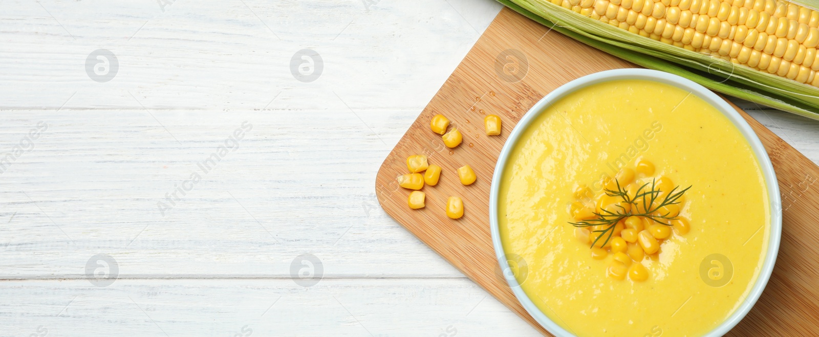 Photo of Delicious creamy corn soup and cob on white wooden table, flat lay. Space for text