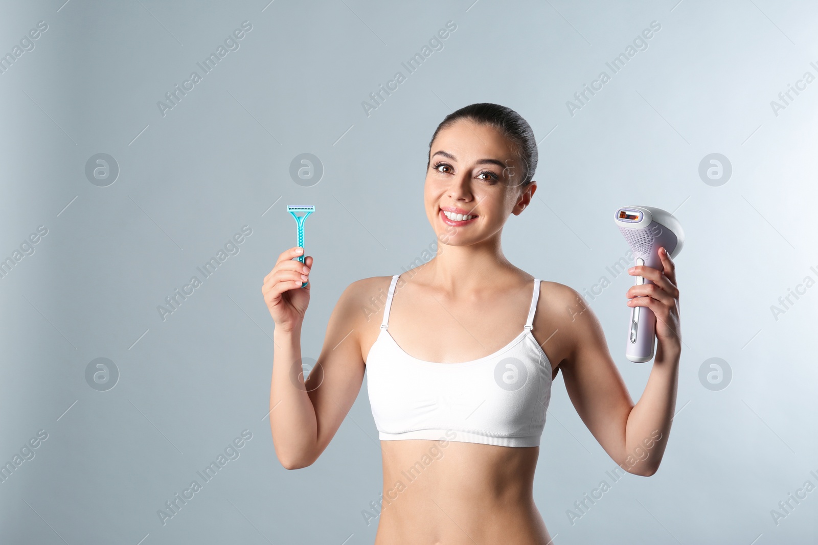 Photo of Beautiful young woman with photoepilator and razor on grey background. Space for text