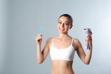 Photo of Beautiful young woman with photoepilator and razor on grey background. Space for text