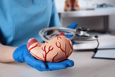 Photo of Gastroenterologist with human stomach model and stethoscope at table in clinic, closeup