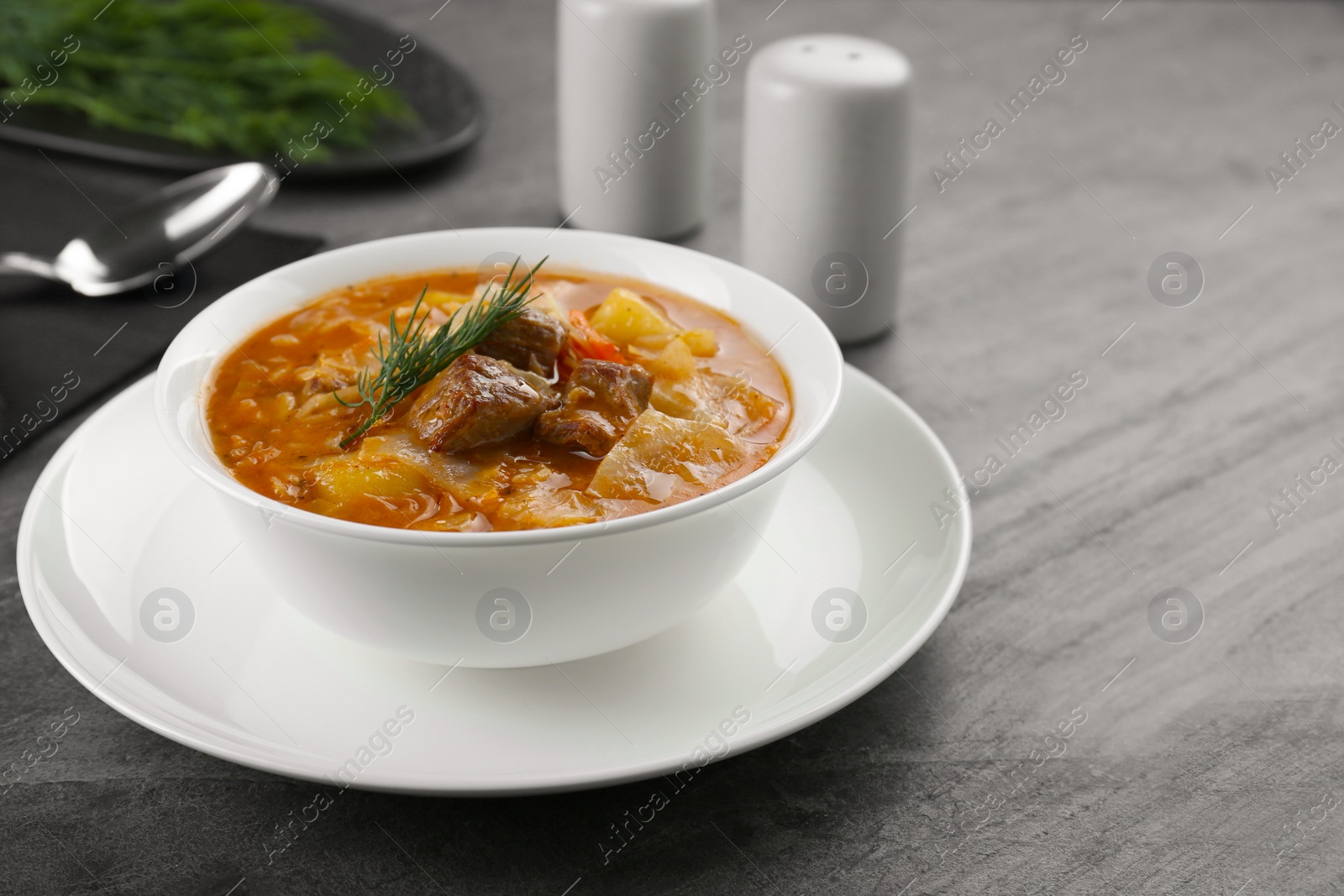 Photo of Tasty cabbage soup with meat, carrot and dill on black table, closeup. Space for text