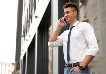 Photo of Portrait of handsome young man talking by phone on city street. Space for text