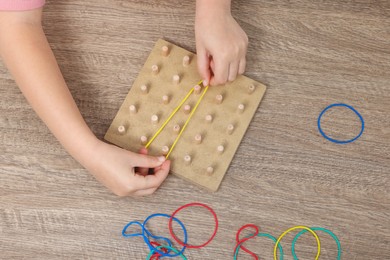 Photo of Motor skills development. Girl playing with geoboard and rubber bands at wooden table, top view