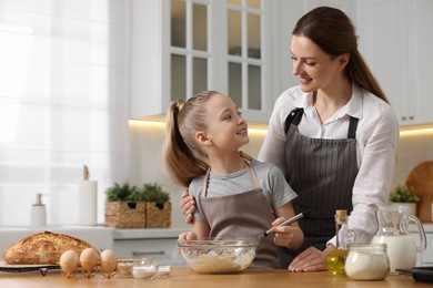 Photo of Making bread. Mother and her daughter preparing dough at wooden table in kitchen