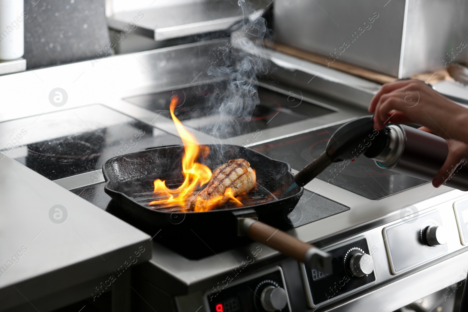 Photo of Female chef cooking meat with manual gas burner on stove in restaurant kitchen, closeup