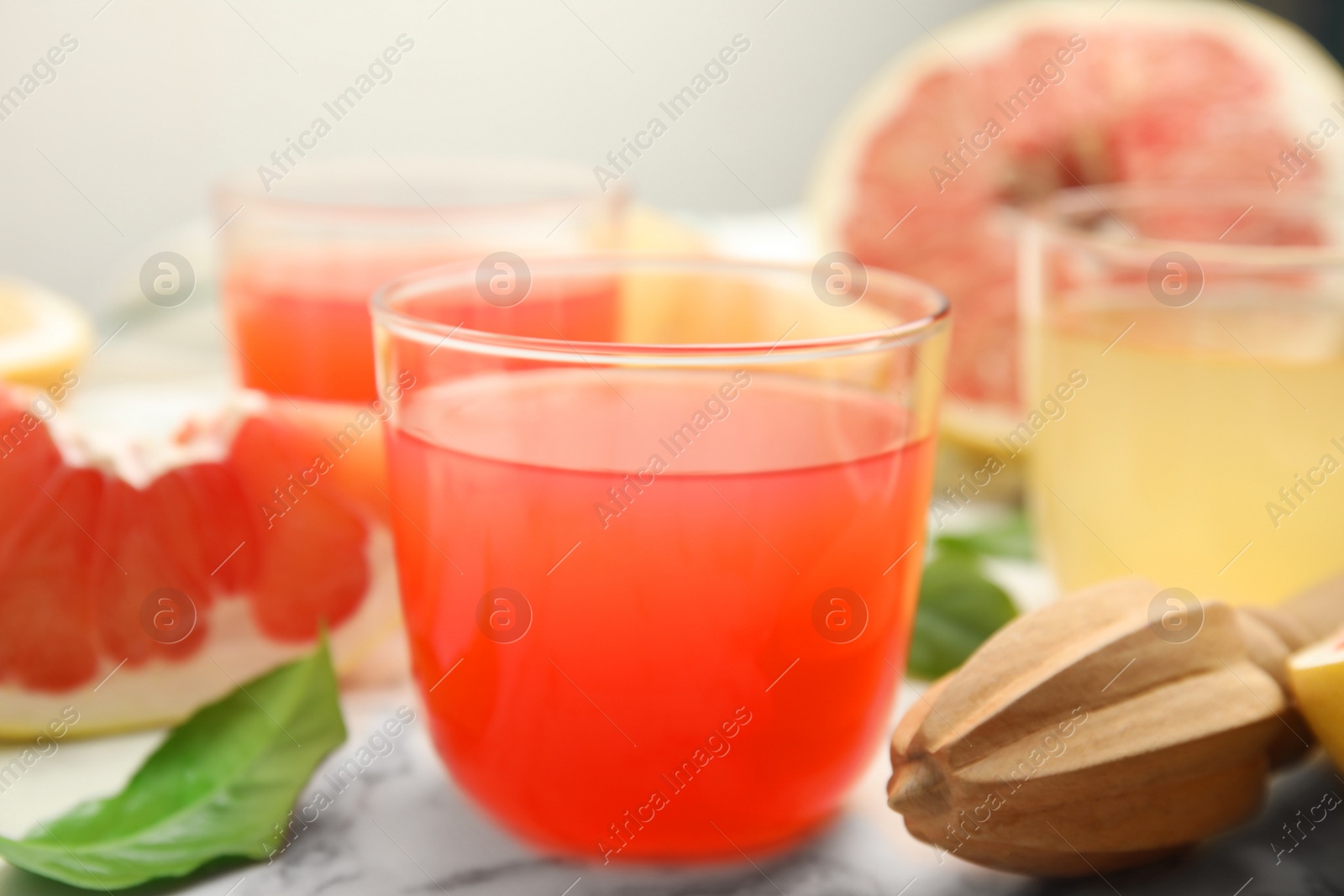 Photo of Glass of pink pomelo juice and reamer on white marble table, closeup