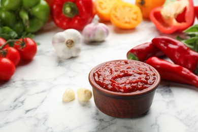 Photo of Delicious adjika sauce in bowl and ingredients on white marble table