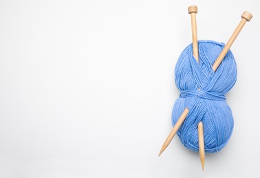 Photo of Soft light blue woolen yarn with knitting needles on white background, top view