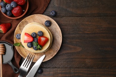 Delicious pancakes with strawberries, blueberries and mint served on wooden table, flat lay. Space for text