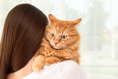 Woman holding adorable red cat on light background