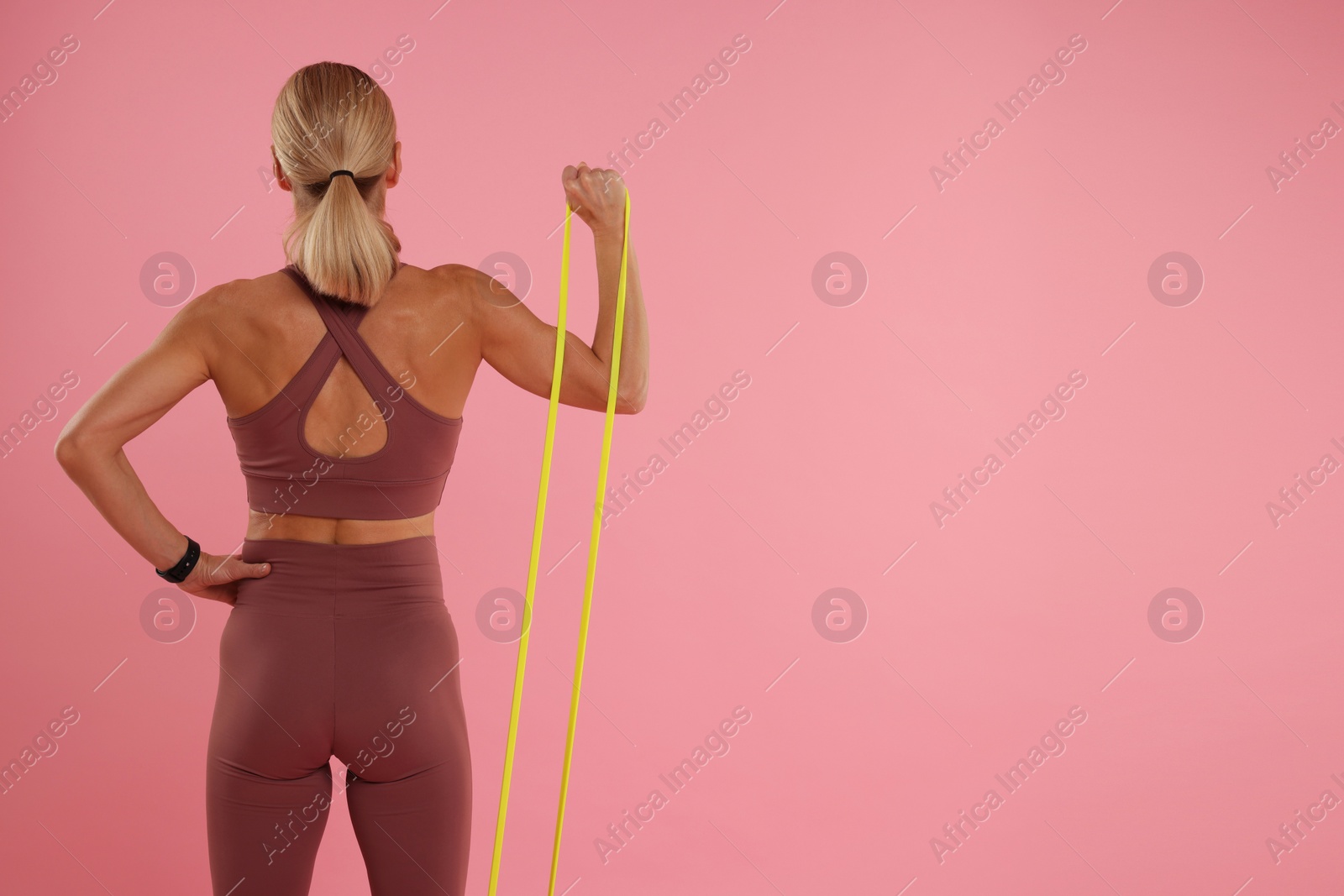 Photo of Woman exercising with elastic resistance band on pink background, back view. Space for text