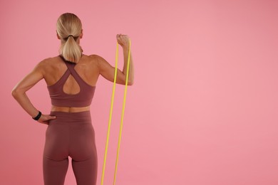 Woman exercising with elastic resistance band on pink background, back view. Space for text