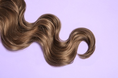 Photo of Lock of brown wavy hair on color background, top view