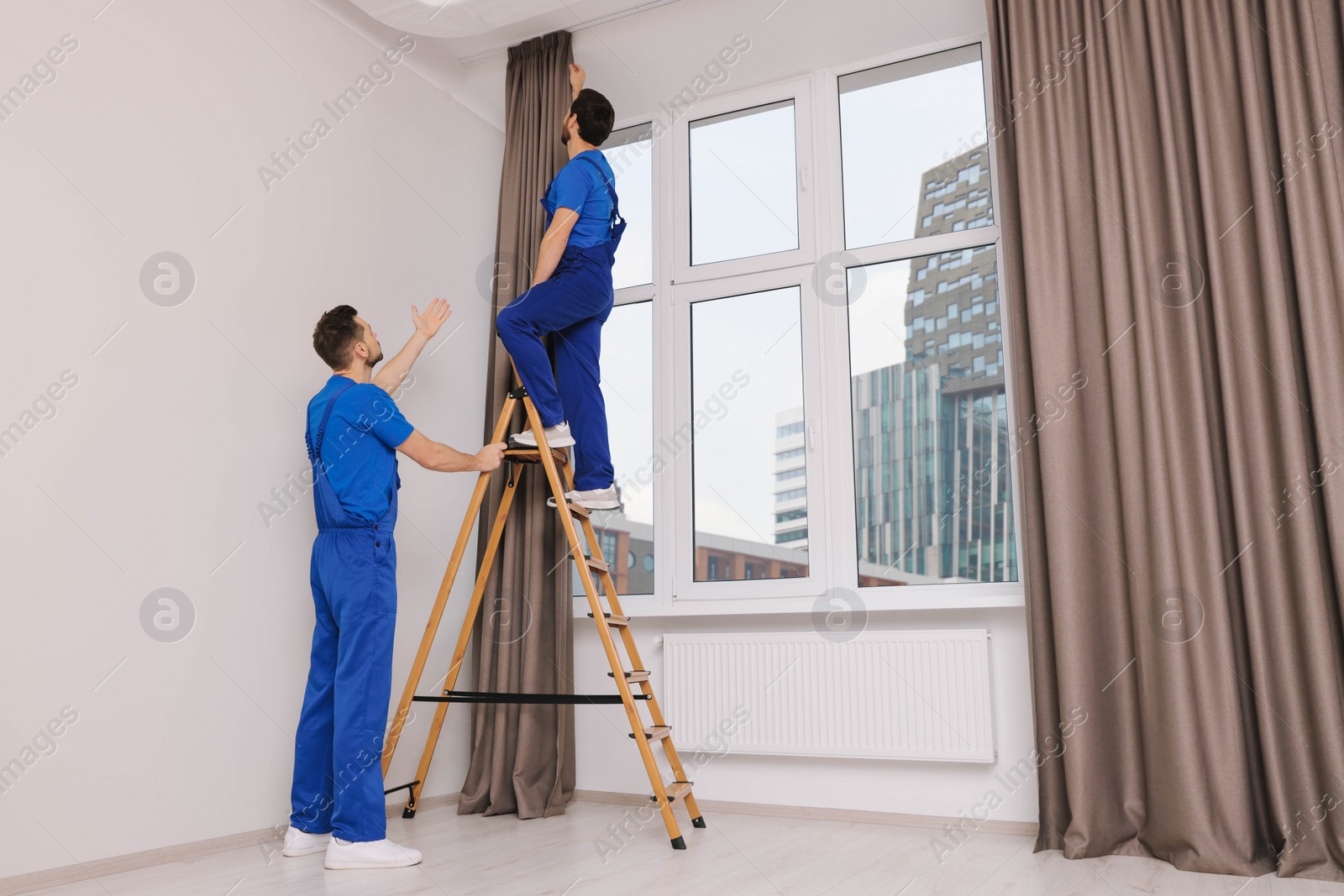 Photo of Workers in uniform hanging window curtain indoors