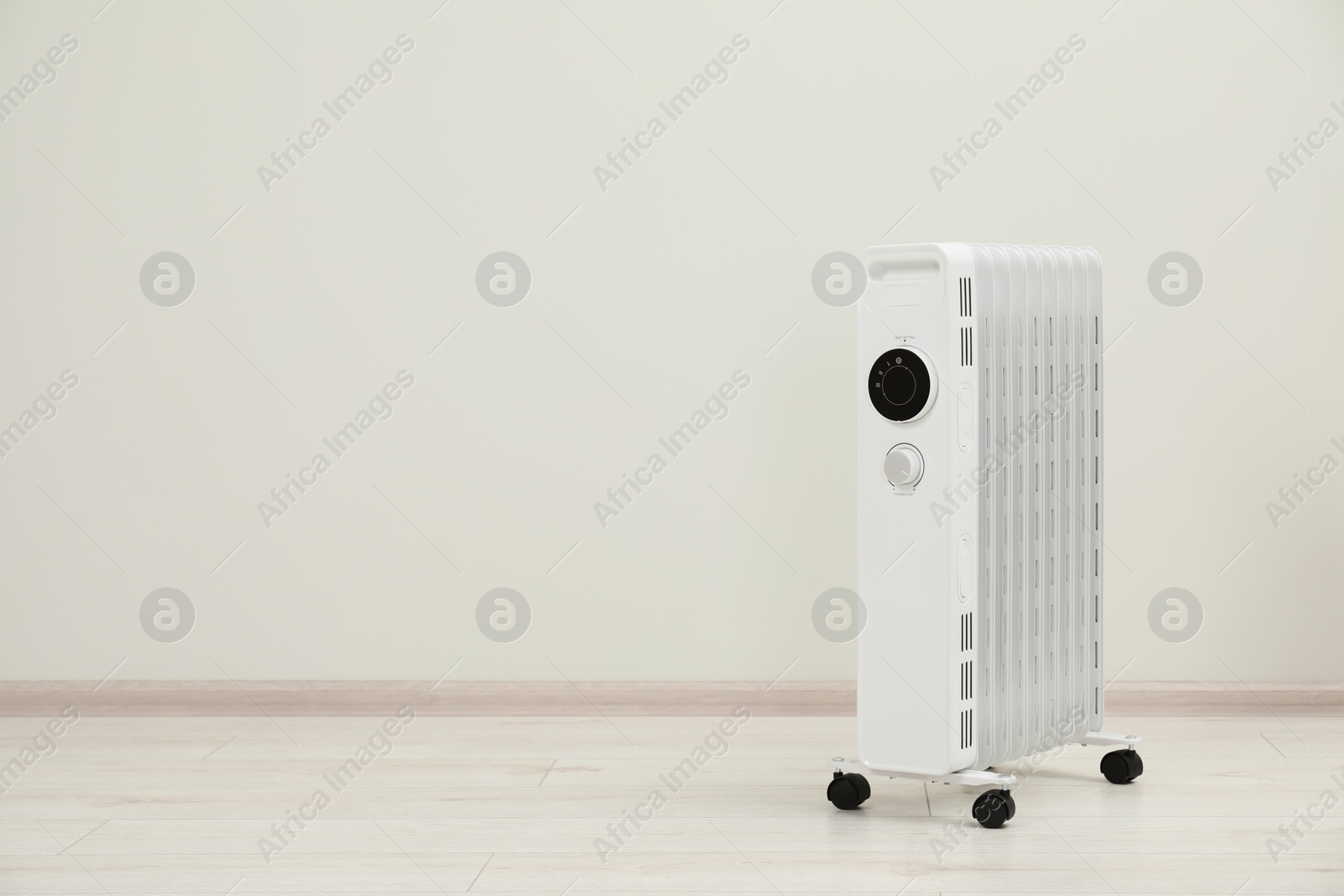 Photo of Modern portable electric heater on floor near white wall indoors, space for text
