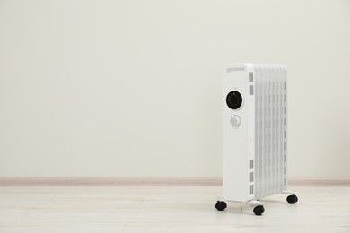 Modern portable electric heater on floor near white wall indoors, space for text