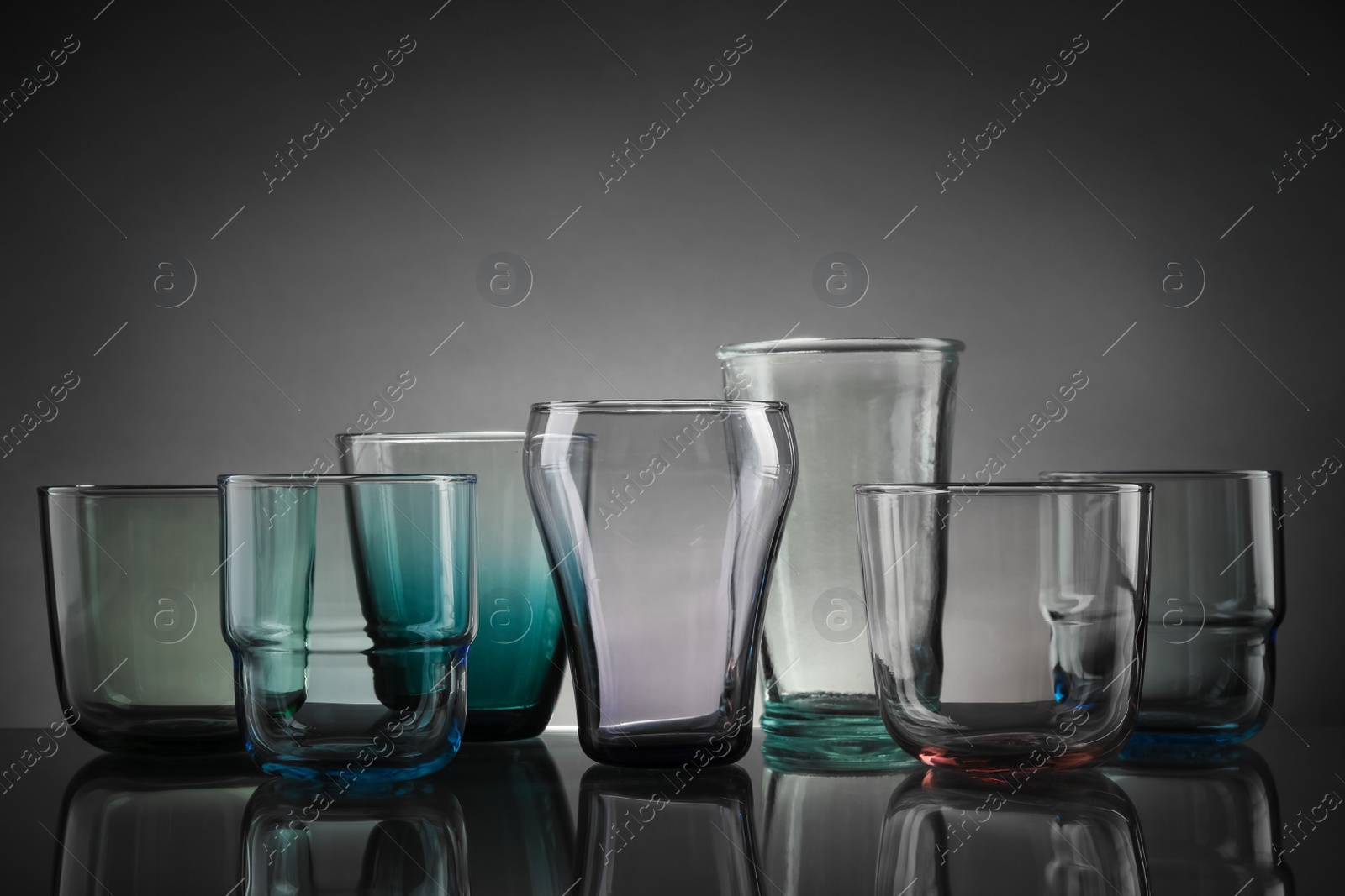 Photo of Set of different colorful empty glasses on table against grey background