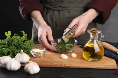 Photo of Woman squeezing garlic with press at black wooden table, closeup