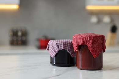 Photo of Jars of jams covered with beeswax food wrap on white table indoors, space for text