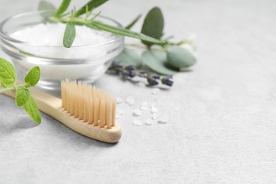 Bamboo toothbrush, sea salt and herbs on light grey table, closeup. Space for text