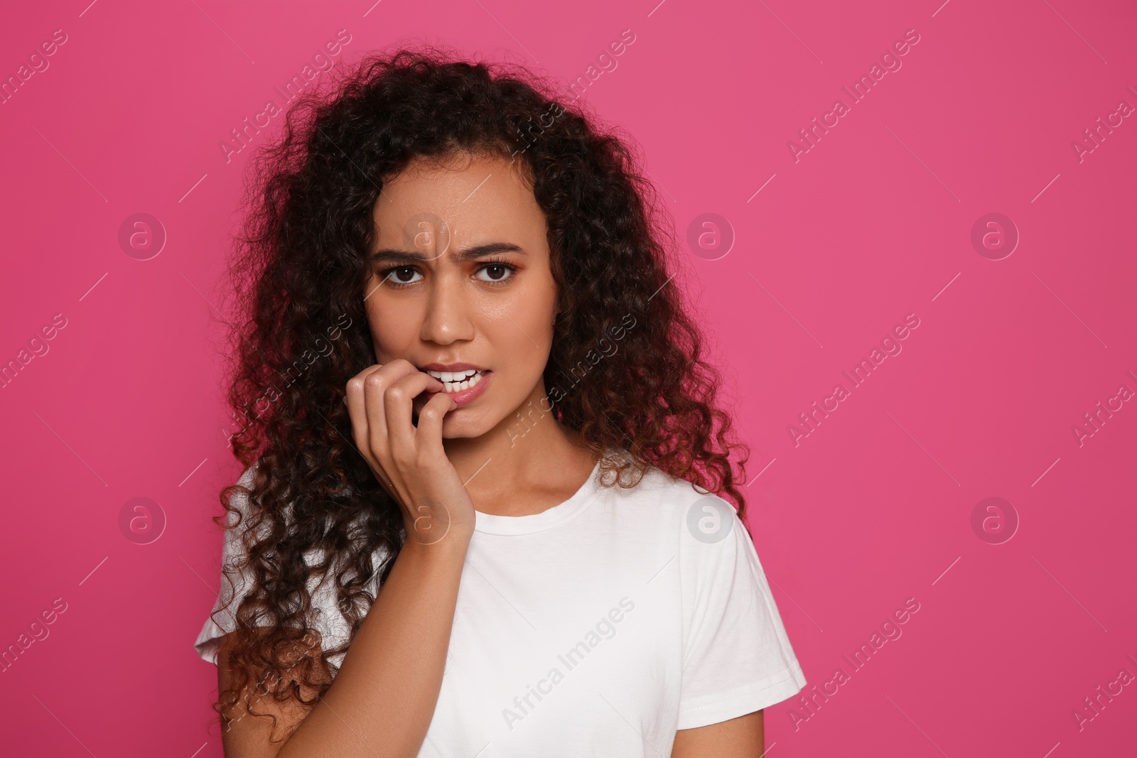 Photo of African-American woman biting her nails on pink background. Space for text