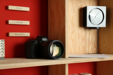 Photo of Stylish wooden shelf with camera and decorative elements on red wall