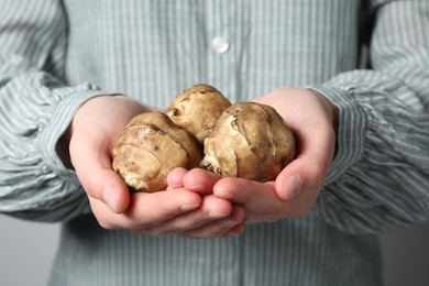 Woman holding Jerusalem artichokes on light grey background, closeup