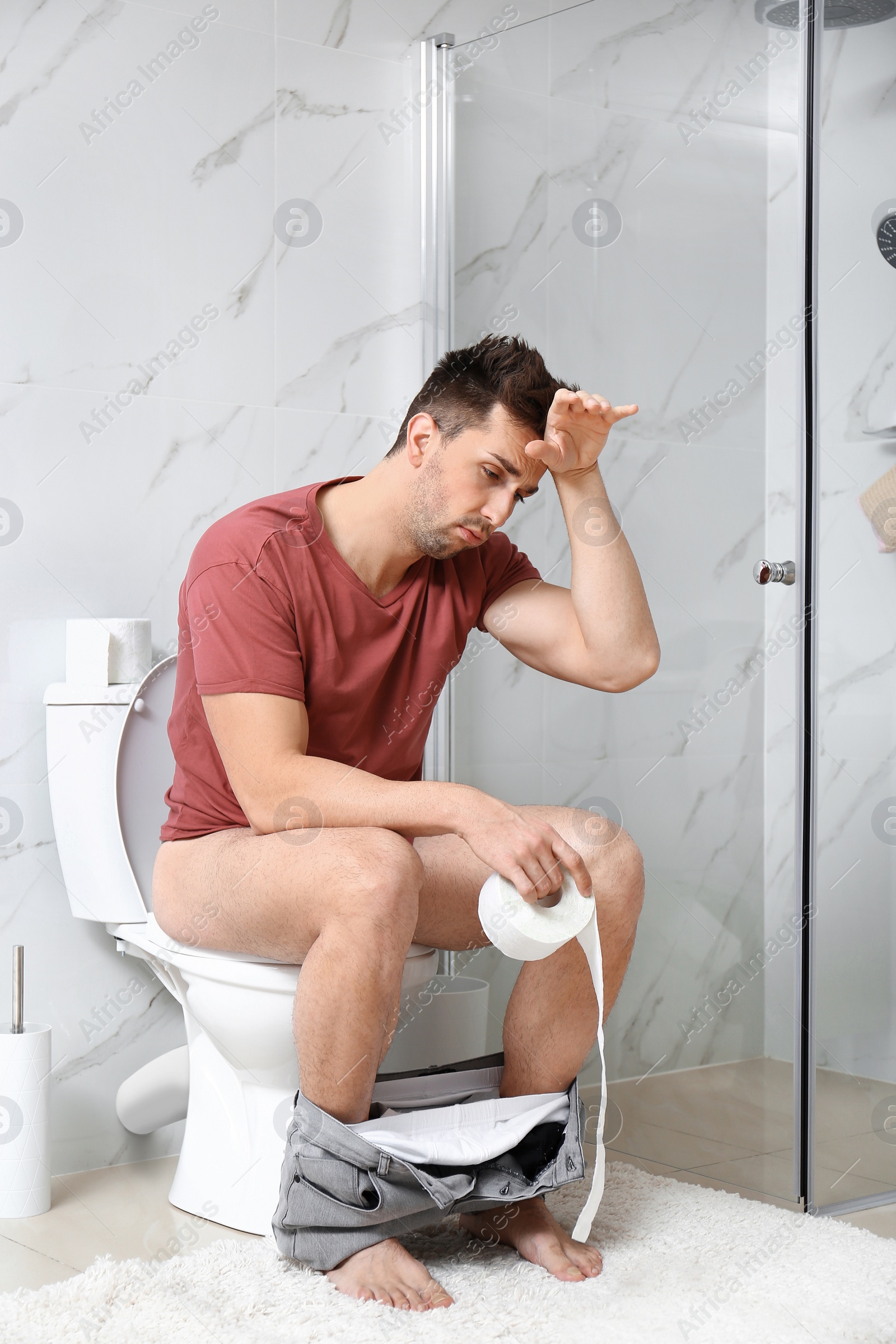 Photo of Man with paper roll sitting on toilet bowl in bathroom