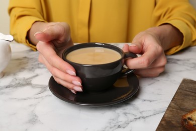 Photo of Woman with cup of aromatic coffee at white marble table, closeup