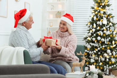 Photo of Happy mature couple in Santa hats with gift box at home. Christmas celebration