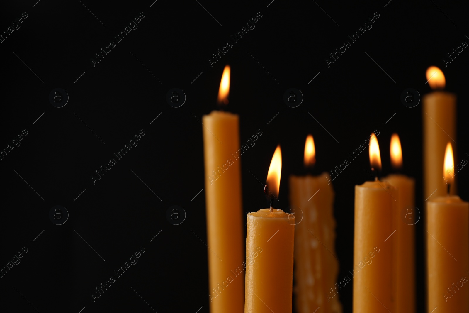 Photo of Many burning church candles on black background, space for text