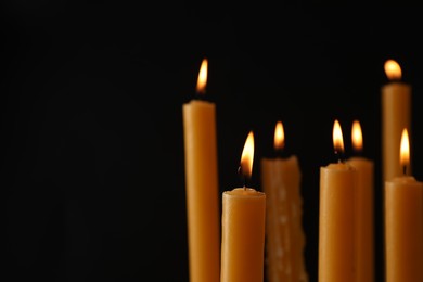 Many burning church candles on black background, space for text